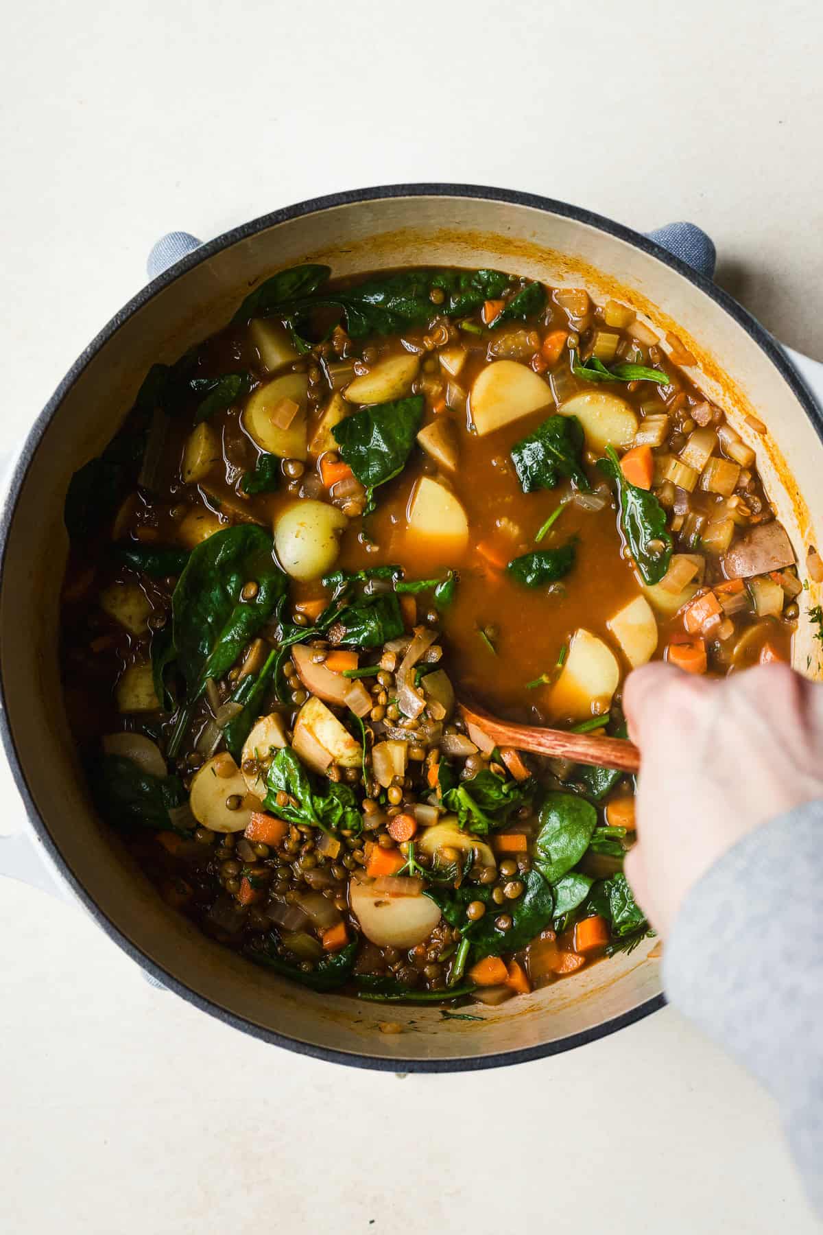Stirring fresh lemon juice into large pot of lentil soup with potatoes.