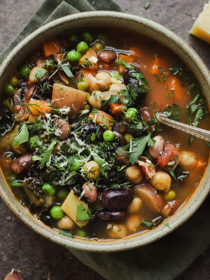 Bowl of spring minestrone with hand scooping a spoonful.