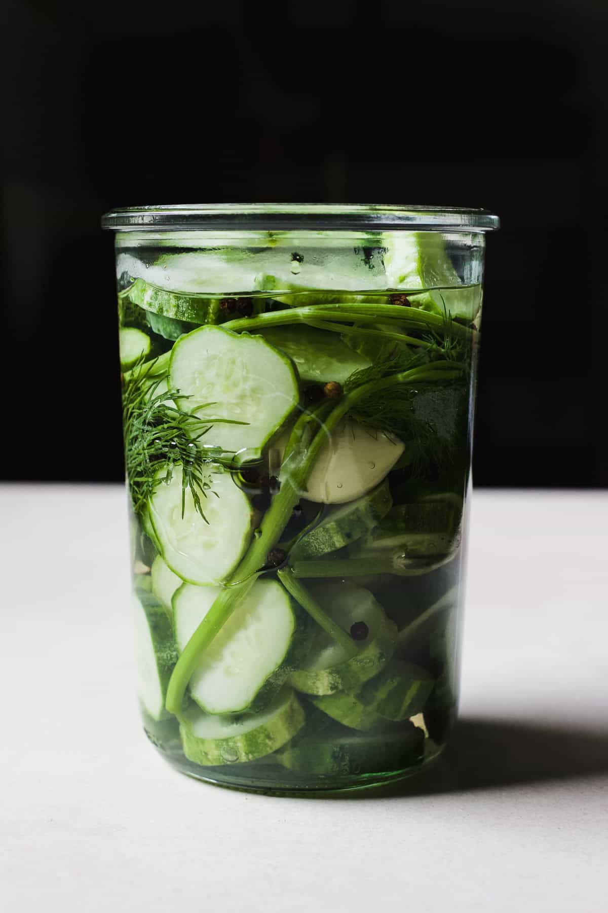 Cucumber refrigerator pickles in a Weck jar with dill, black peppercorns, and garlic.