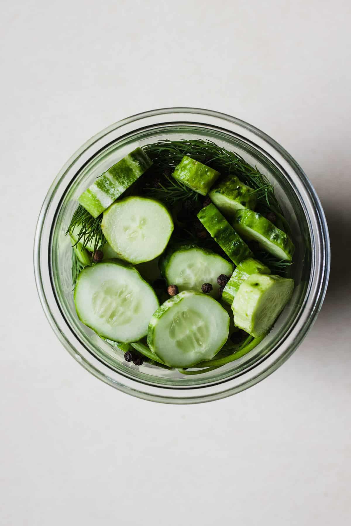Cucumbers, dill, garlic, black peppercorns, and salt in a jar for pickling.
