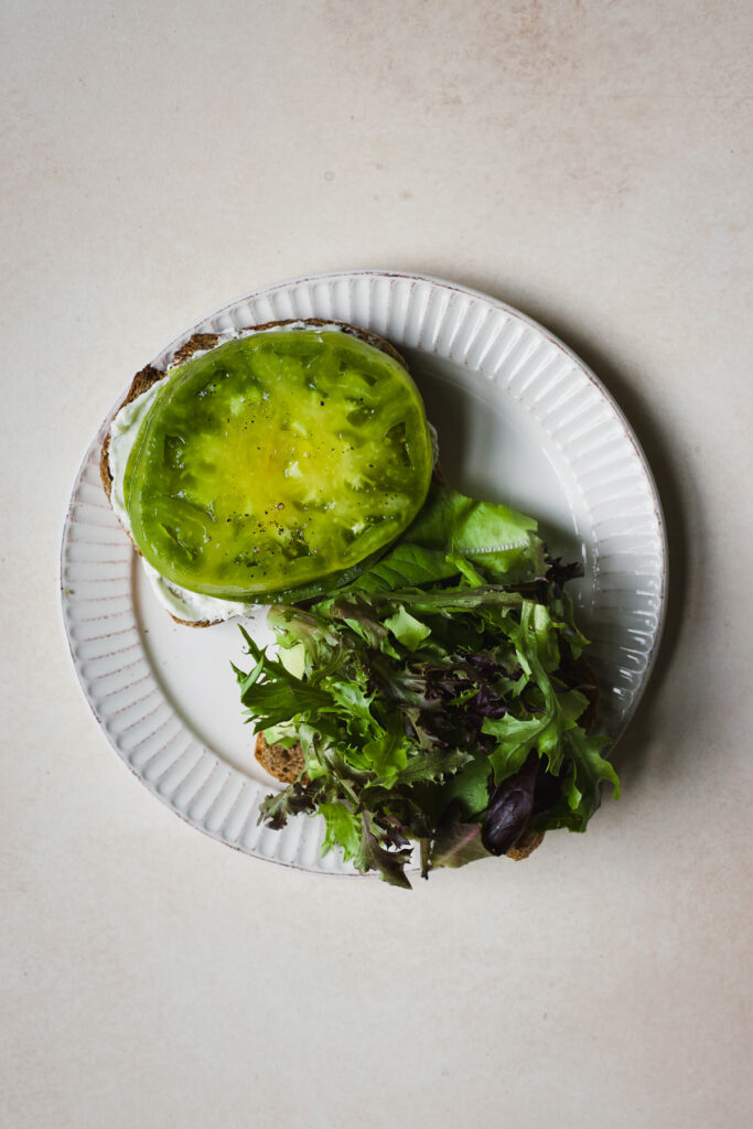 Each sandwich half being assembled with thick tomato slices and mixed greens.