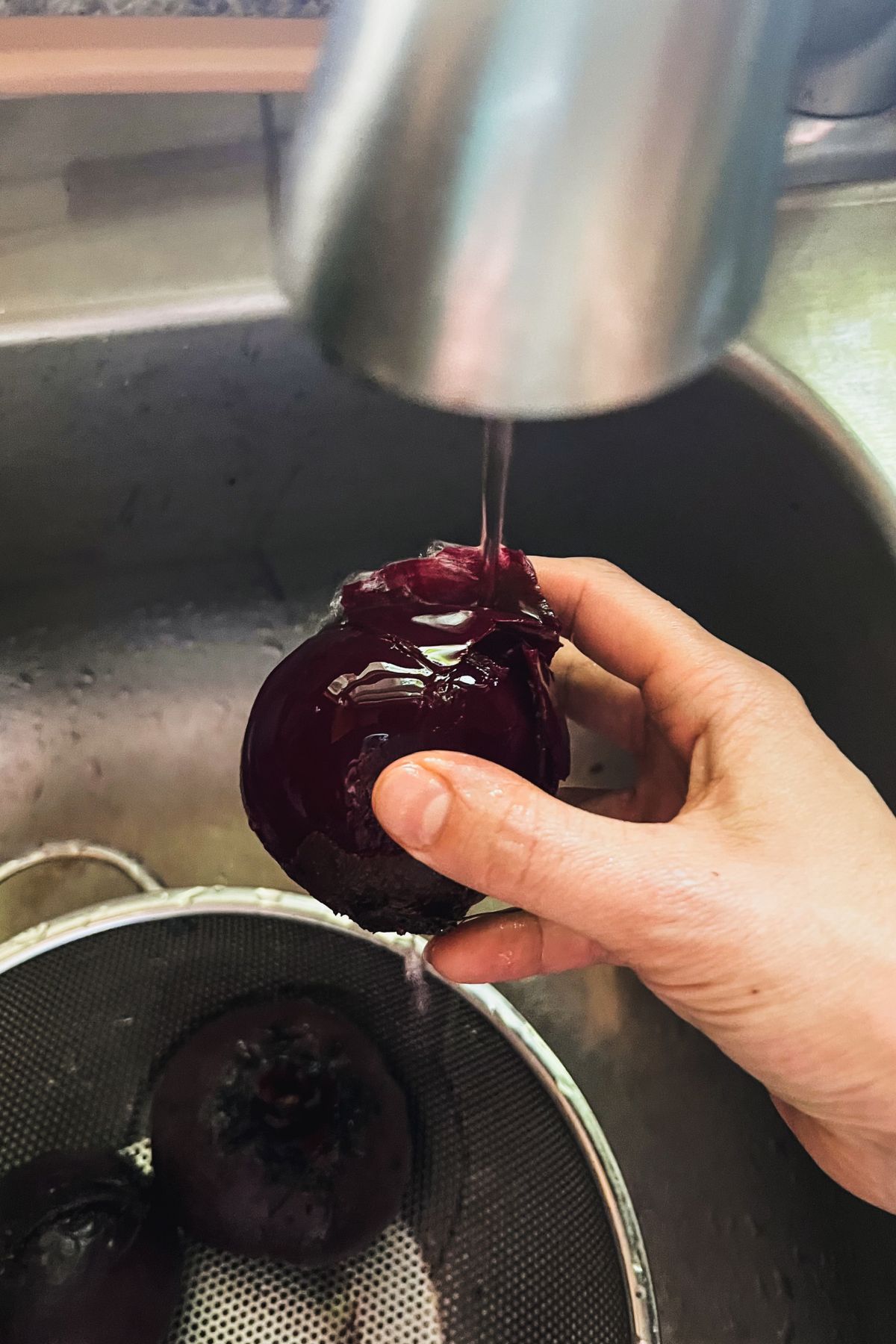Peeling a beet under running water from the faucet.