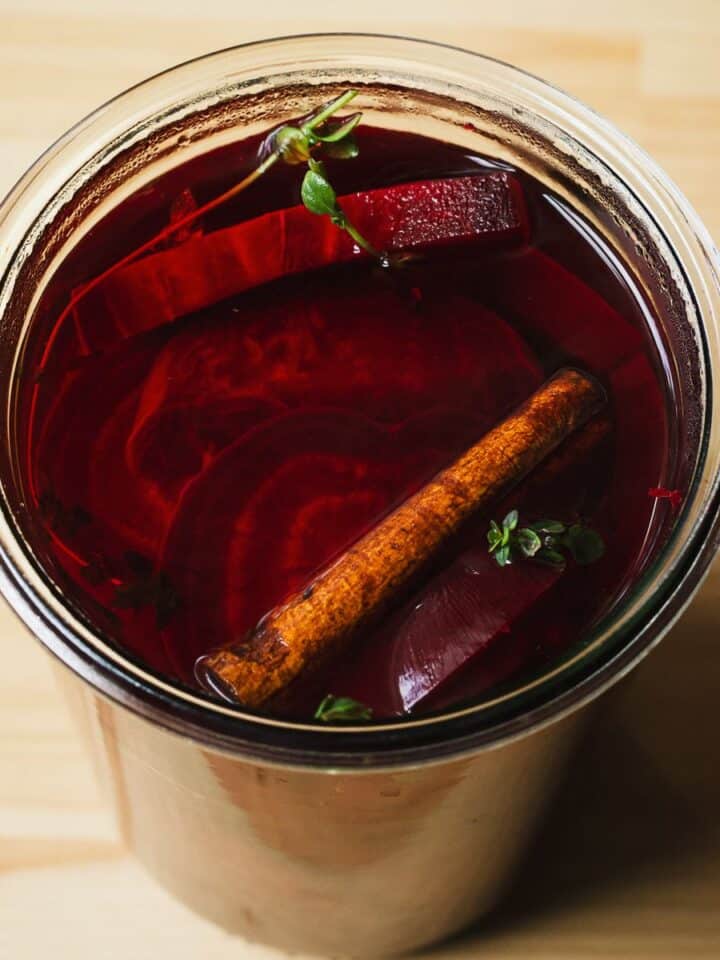 Pickled beets in a jar with cinnamon stick and thyme.